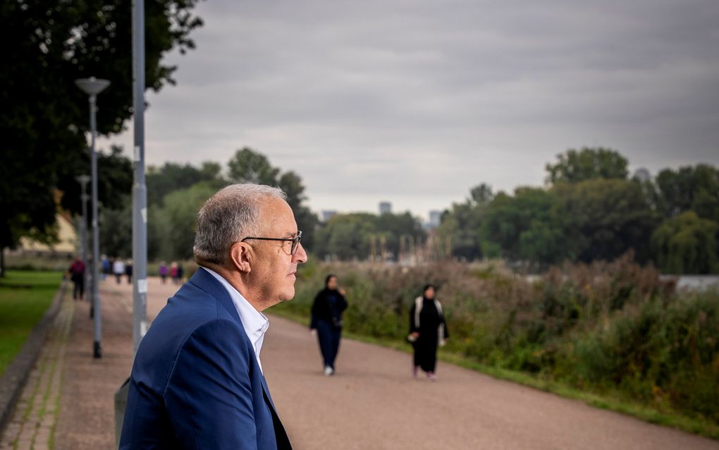 Man zit op de rugleuning van een bankje. In de verte komen twee gesluierde vrouwen aanlopen.