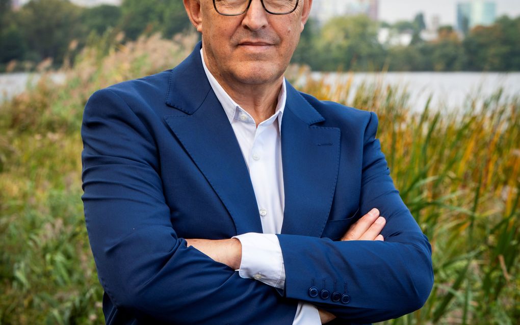 Man poseert met de armen over elkaar. Hij draagt een blauw pak zonder stropdas.