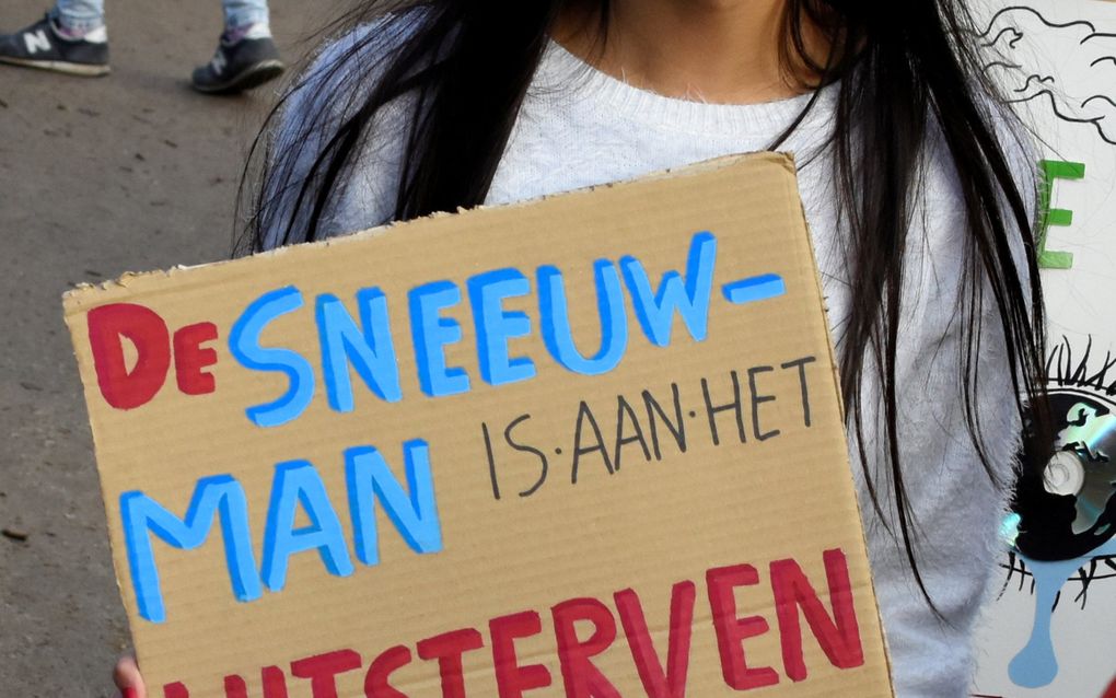 Meisje met zwart haar houdt een kartonnen bord vast waarop staat: De sneeuwman is aan het uitsterven, doe iets!!