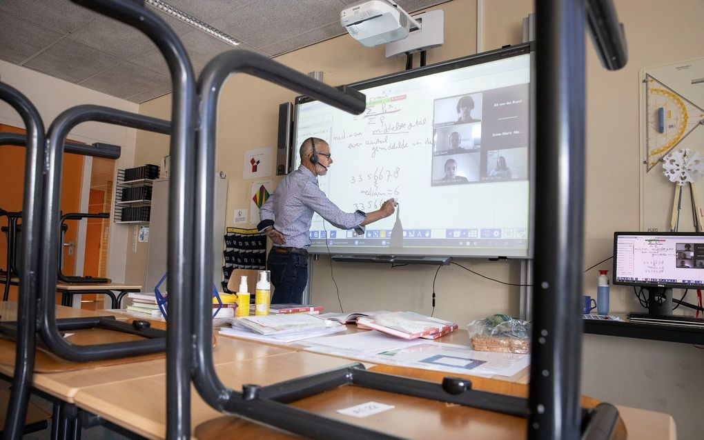 Ab van der Roest, docent op het Ichthus College in Veenendaal, geeft vanuit een leeg lokaal les. Via het programma Zoom kunnen de leerlingen thuis de uitleg volgen. beeld RD, Anton Dommerholt