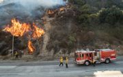 Brandweermannen houden een stuk brandende natuur in Newhall, Californië in de gaten. beeld AFP