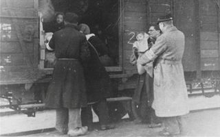 Zwart-witfoto uit de Tweede Wereldoorlog. Een man staat met een baby in zijn armen bij de open deuren van een trein. Vanuit de wagon kijkt een ander kind naar buiten.