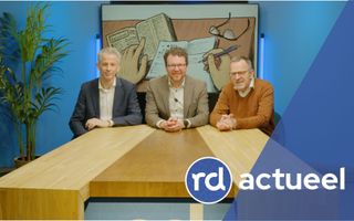 Drie mannen achter een tafel. 