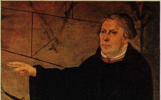 Afbeelding van een man in zwart kleed op een preekstoel. Voor hem ligt een Bijbel.