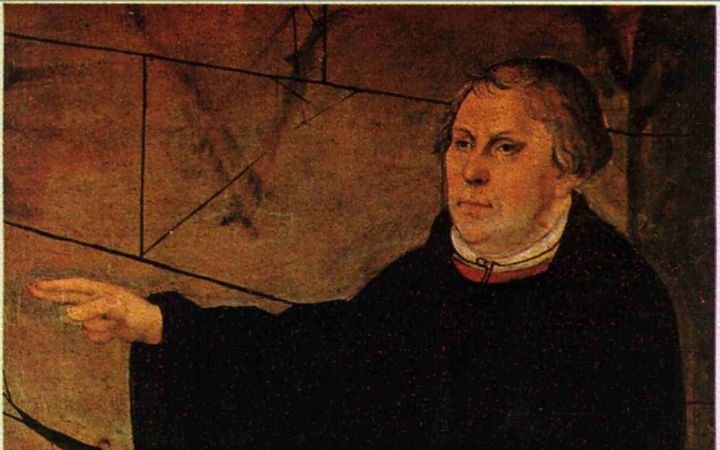 Afbeelding van een man in zwart kleed op een preekstoel. Voor hem ligt een Bijbel.