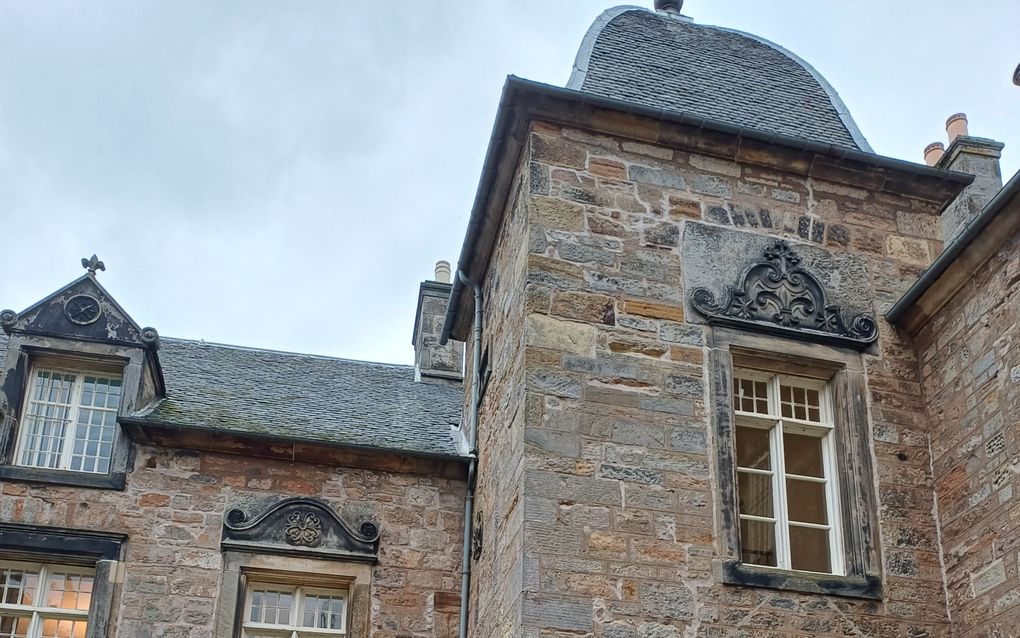 Oud gebouw met aan de rechterkant een toren. Op de trappen voor de toegangsdeur zitten twee vrouwen.