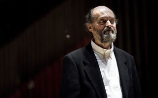 Oudere man met grijze baard in een zwart colbert met daaronder een wit overhemd. Hij kijkt weg van de camera.