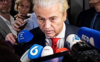 Man met achterover gekamd, blond haar spreekt in microfoons van een aantal nieuwsmedia.