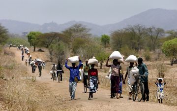 Mensen lopen met witte zakken op hun hoofd in een droog landschap