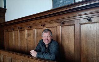 Een glimlachende man met grijzend haar in een oude kerkbank.