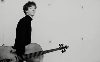 Een zwart-witfoto van een jonge cellist die loopt en zijn instrument draagt.