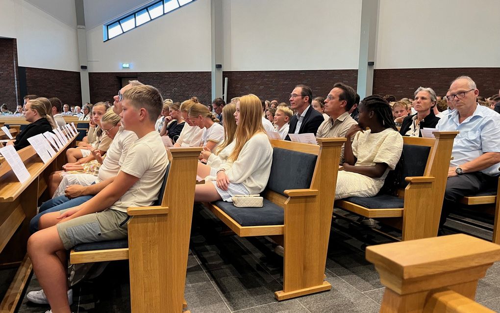 Jongeren en hun ouders zitten in kerkbanken. 