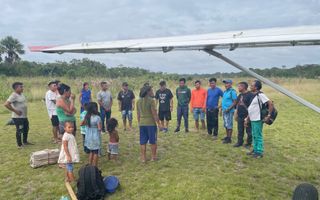 Een groep gekleurde mensen staat op een grasveld bij een vliegtuig.