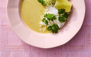 Een lichtroze diep bord met geel-groene soep en hoopjes rijst en rauwkost.