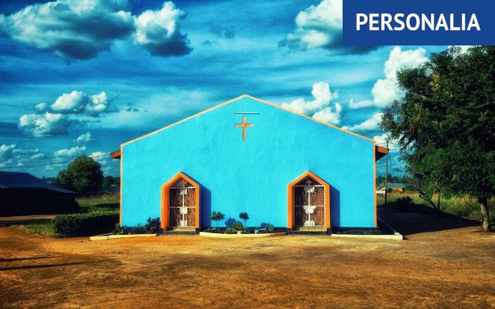 Een eenvoudig, blauwgeschilderd kerkje in een landelijke omgeving.