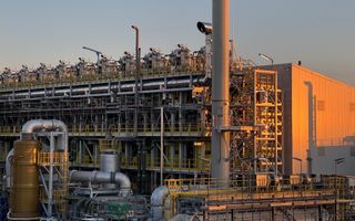 Fabriek met veel buizen en geel hekwerk.