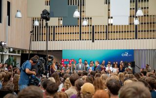 Een zaal vol mensen, achterin staat een camperaploeg.