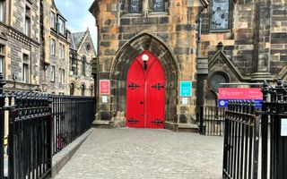 Voorgevel van een uit geelgrijze stenen opgebouwd kerkgebouw. De deuren zijn rood geverfd.