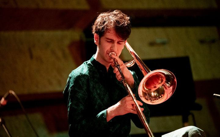 Een jonge muzikant speelt trombone met zijn ogen dicht.