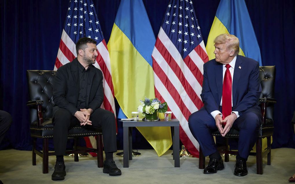 Twee mannen zitten op donkere stoelen. Achter hen hangen gekleurde vlaggen.