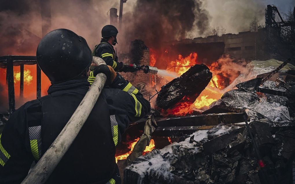 Twee mannen richten een waterslang op een vuurzee.