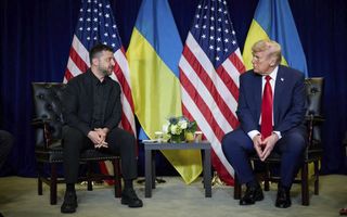 Twee mannen zitten op donkere stoelen. Achter hen hangen gekleurde vlaggen.