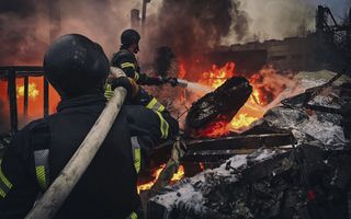 Twee mannen richten een waterslang op een vuurzee.