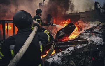 Twee mannen richten een waterslang op een vuurzee.