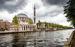 Een moskee met een minaret, gelegen aan een kanaal.
