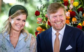 Man in pak met oranje stropdas en vrouw met groene hoed en blauwe jurk met groene tinten.