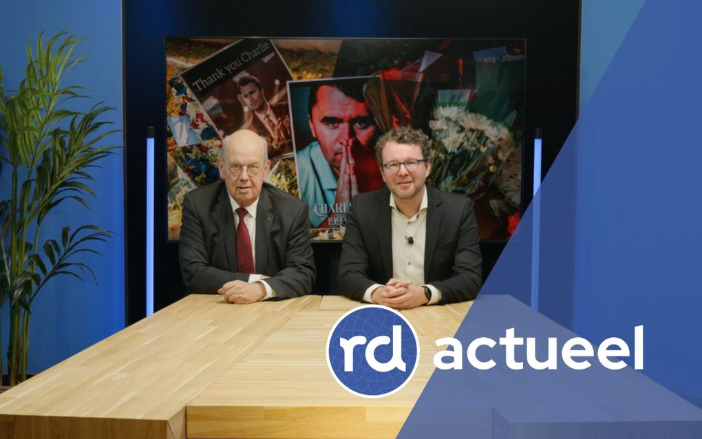 Twee mannen in donkergrijs pak zitten aan een houten tafel.
