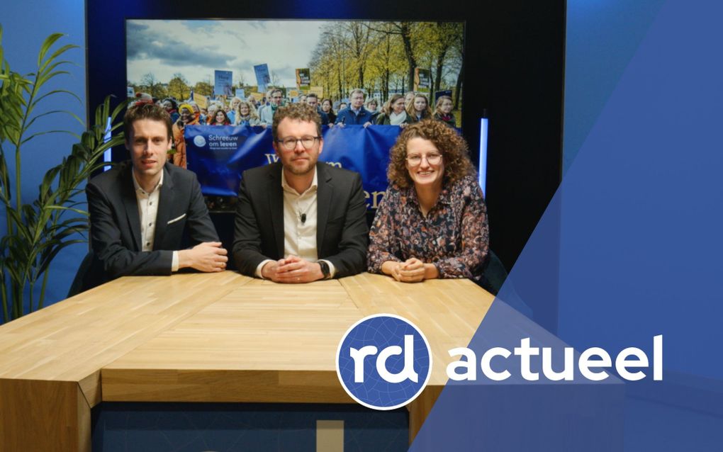 Twee mannen en een vrouw zitten achter een houten tafel.