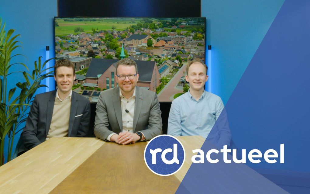 Drie mannen van middelbare leeftijd zitten vriendelijk lachend achter een houten tafel.