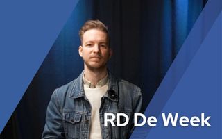 Een man staat voor een blauwe achtergrond.