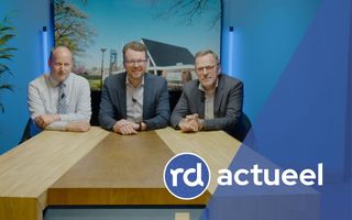 Drie net geklede mannen zitten aan een houten tafel.