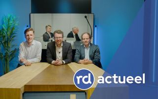 Drie net geklede mannen zitten aan een houten tafel.