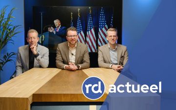 Drie mannen in overhemd en colbert zitten aan een houten tafel.