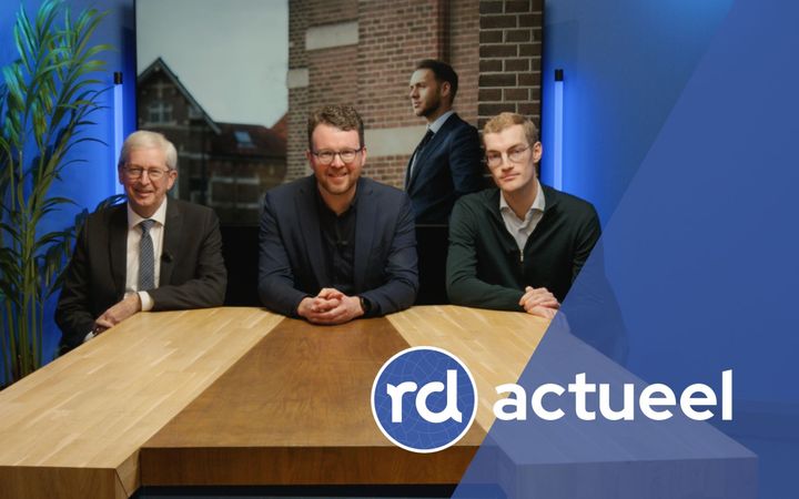 Drie mannen zitten aan een houten tafel.