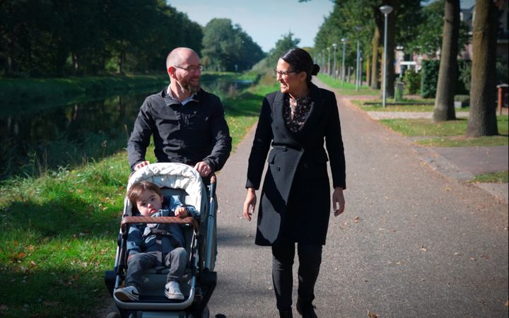 Vader en moeder met kindje in wandelwagen wandelen buiten. 