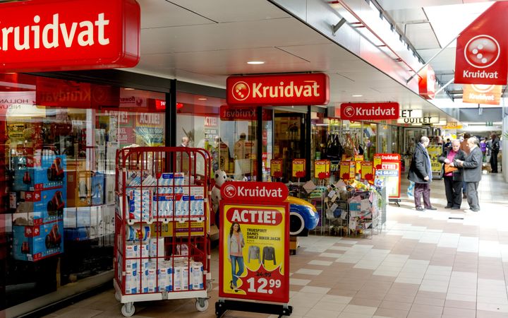 Rode borden met daarop het woordje Kruidvat staan voor een winkelpand. Op de stoep staan allerlei producten opgesteld.