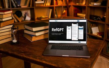 Een laptop op een bureau, met daarachter boeken op stapels en boeken in een kast.