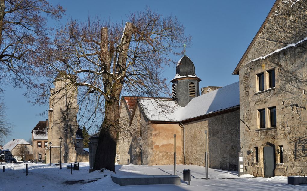 Straatbeeld met bomen, huizen en een kerk. Er ligt sneeuw.