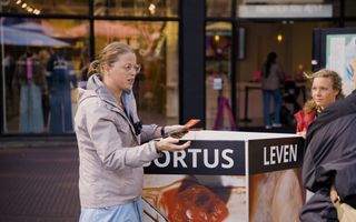 Een vrouw staat in een winkelstraat bij een bord met foto’s van een geaborteerd kindje. Ze is in gesprek met een vrouw.
