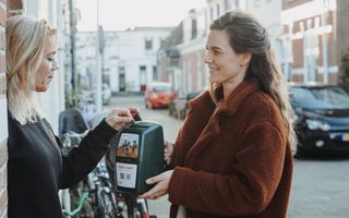 Een vrouw haalt geld op met een collectebus van ZOA. Een andere vrouw stopt een euromunt in de collectebus. 