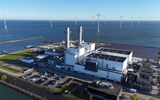 Energiecentrale met twee schoorstenen op een soort eiland in een grote wateroppervlakte waarin ook windmolens staan. 