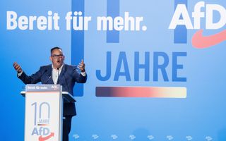 Man in blauw pak zonder stropdas gebaart tijdens zijn toespraak. Op de achtergrond een blauw vlak met de tekst: Bereit für mehr Jahre (Klaar voor nog vele jaren)  AfD