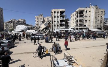 Straatbeeld in Gaza. Tientallen mensen bevinden zich op een open terrein. Op de achtergrond witte, deels verwoeste flatgebouwen en witte tenten.