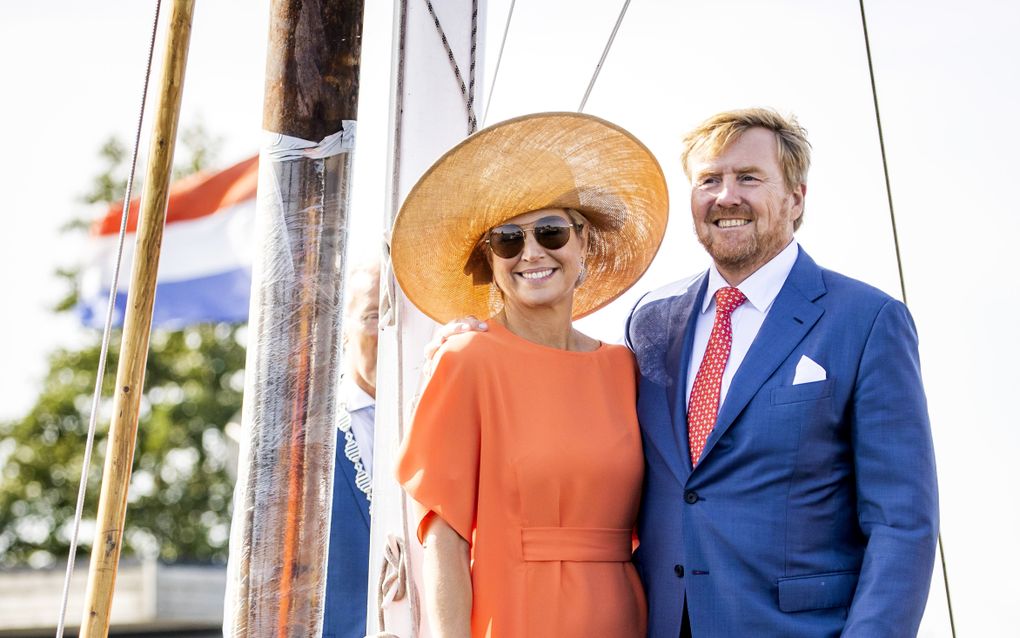 Een vrouw in een oranje jurk en hoed staat naast een man in een blauw pak op een zeilschip.