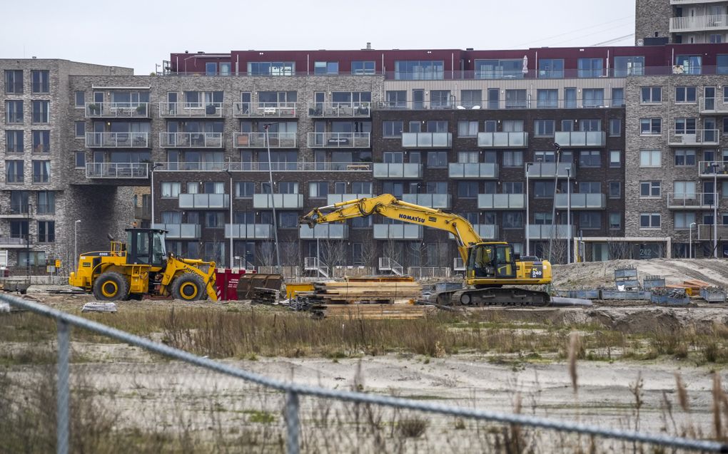 Voor een stel nieuwe appartementen staan een gele shovel en een gele kraan te wachten tot ze weer aan het werk kunnen. 