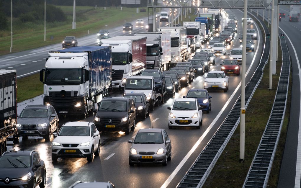 Auto’s met koplampen aan staan in drie rijen op de snelweg in de file bij regenachtig weer.